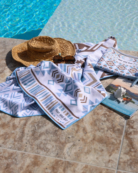 Light blue towel with geometric pattern, straw hat, and wetbag by a poolside.