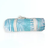 Nap and Sun Leafy Vibe light green picnic blanket rolled up, secured with a white/beige carry strap.