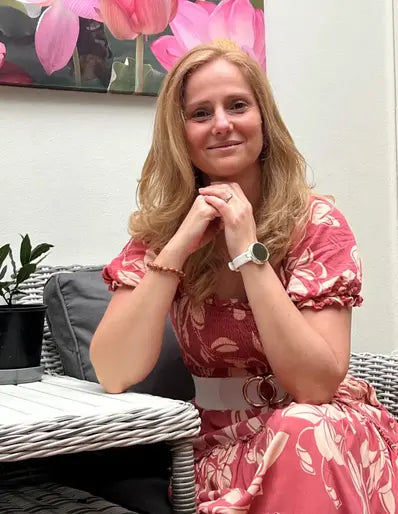 Andrea in a red dress, sitting in a chair, facing the camera and smiling warmly.