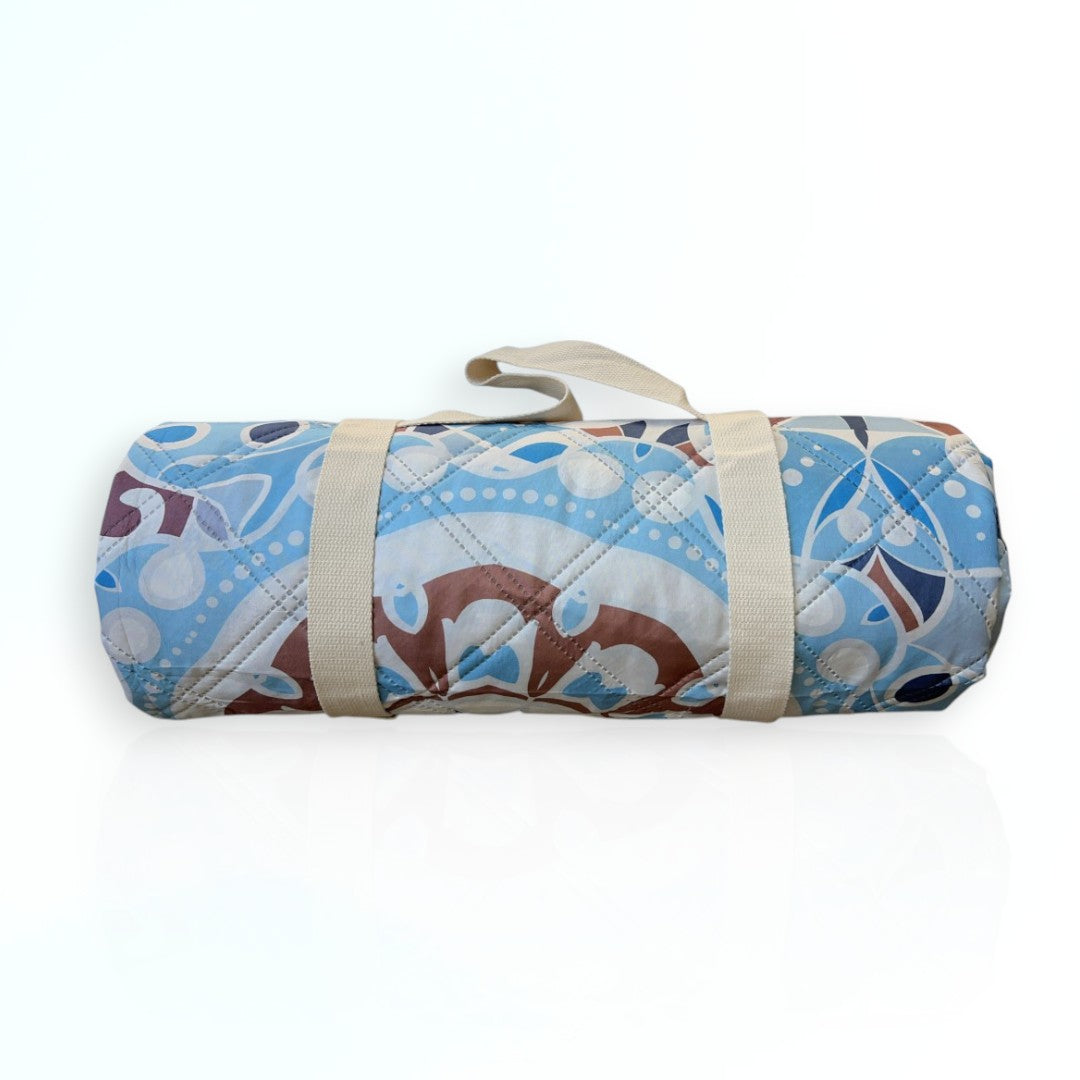 Nap and Sun Mandala Magic pattern picnic blanket rolled up with a beige carry strap securely attached around it.