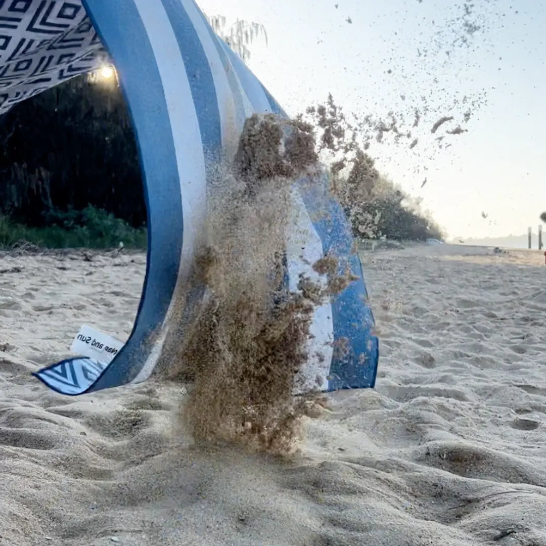 Shaking the blue white striped towel on the beach, sand flying off for a clean and easy experience.