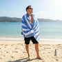 Man wrapped in a blue and white striped towel on a beach with clear blue water in the background.
