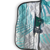 Close-up of the zip pocket on a light green palm leaf-patterned picnic blanket, holding a phone and car key.