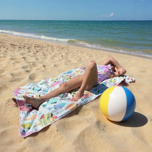 a girl lying on a colorful beach towel with a beach ball next to them on a sandy beach.