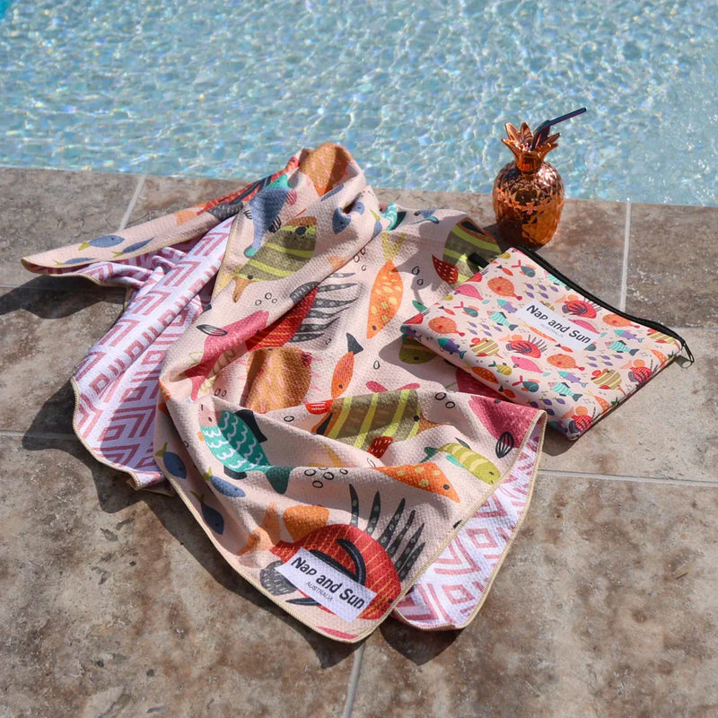A colorful fish-print beach towel lies beside the pool.
