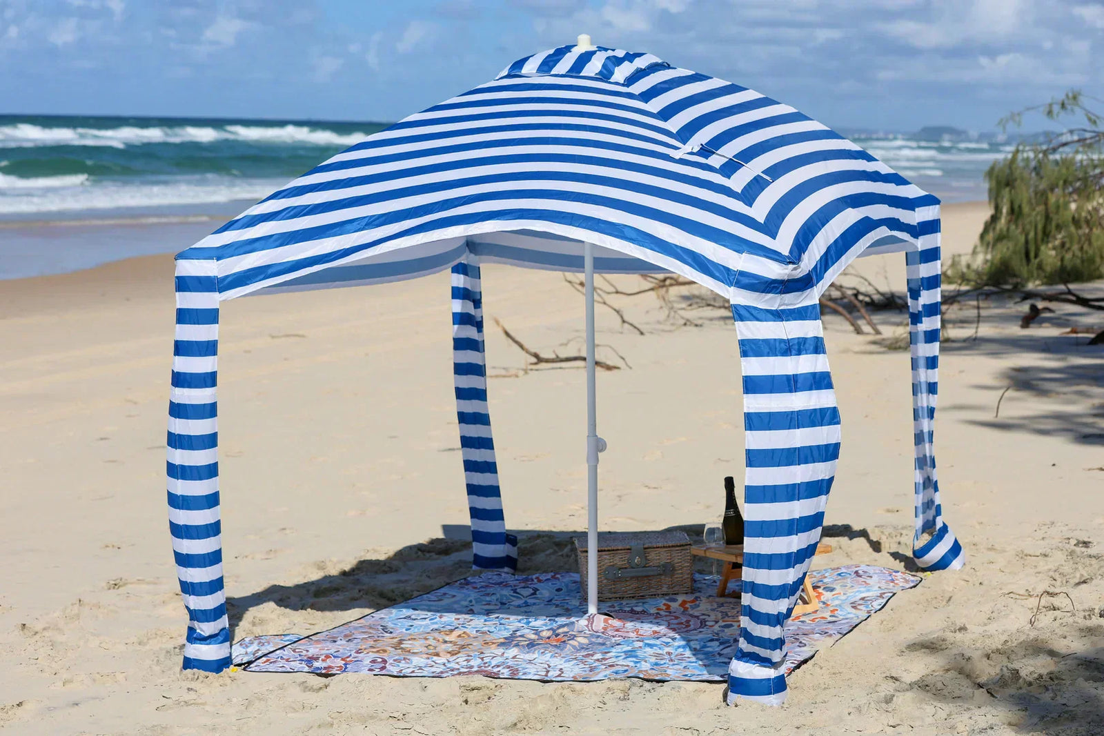 patterned picnic blanket with cabana on a sandy beach.