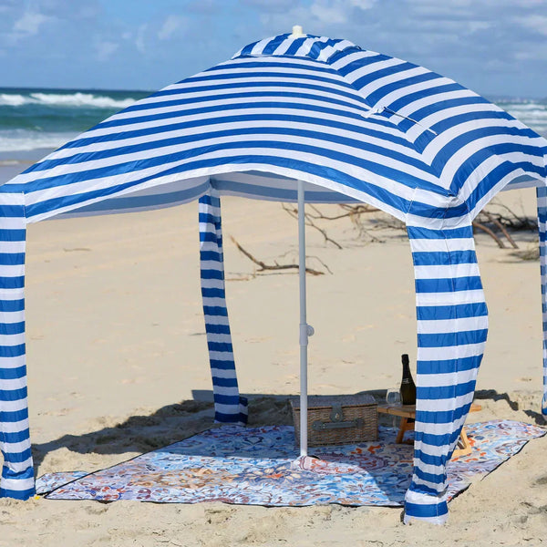 patterned picnic blanket with cabana on a sandy beach.