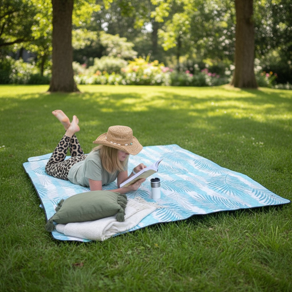 Woman is lying on a picnic blanket and reading in a park.