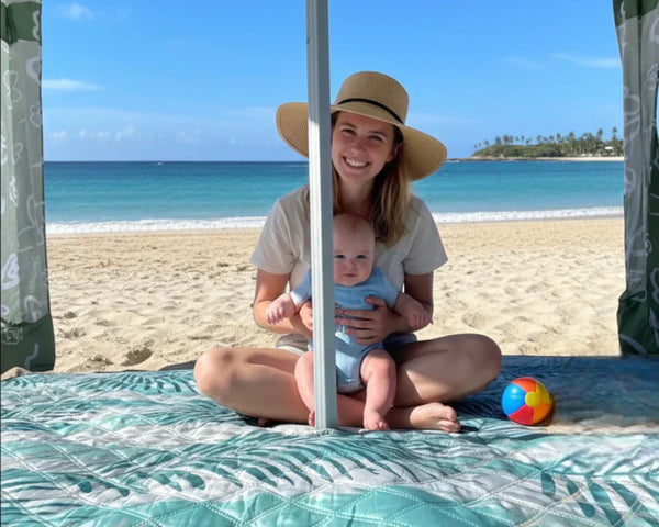 woman and her baby is sitting on a beach blanket on a beach