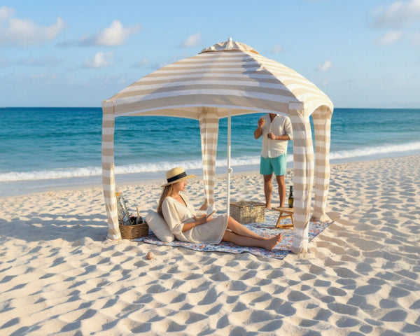 woman is reading on a beach mat under a cabana on the beach