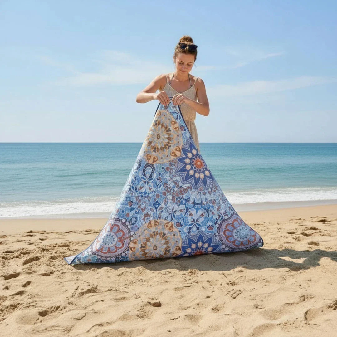 woman is folding a mandala pattern picnic blanket on the beach
