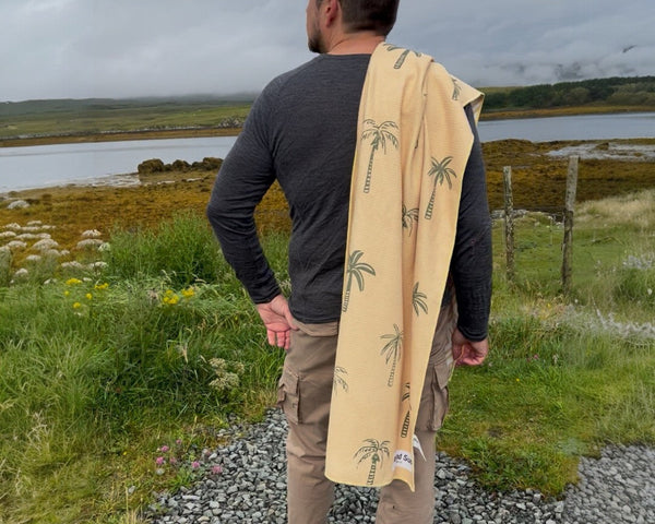 Man overlooking a lake on a rainy day with a yellow palm tree patterned towel draped over his shoulder.