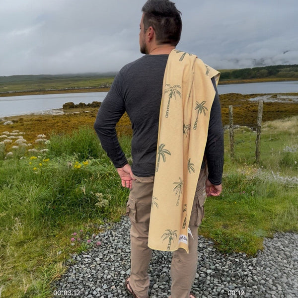 Man overlooking a lake on a rainy day with a yellow palm tree patterned towel draped over his shoulder.