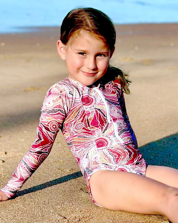 Young girl in a colorful swimsuit sitting on a sandy beach.