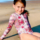 Young girl in a colorful swimsuit sitting on a sandy beach.