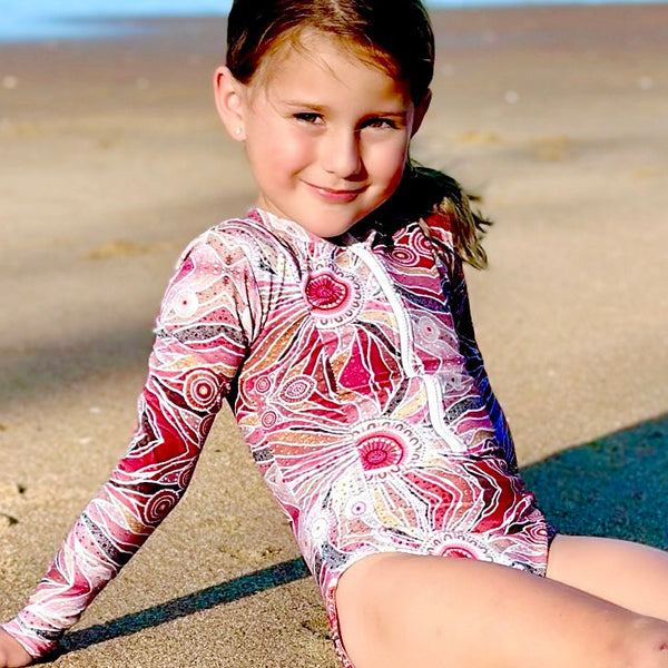 Young girl in a colorful swimsuit sitting on a sandy beach.