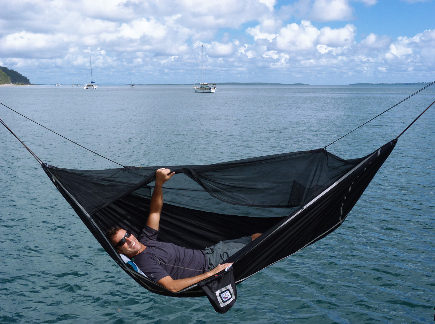 Person relaxing in a black hammock over a body of water 