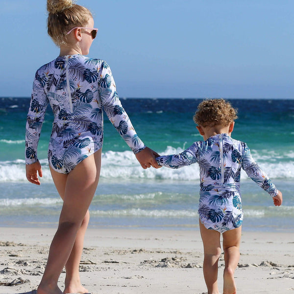 Two children in matching UV50+ swimsuits walking on a beach 