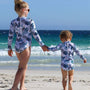 Two children in matching UV50+ swimsuits walking on a beach 