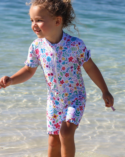 Child in a floral swimsuit standing in shallow water at the beach