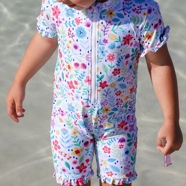 Child wearing a colorful floral swimsuit on a beach.