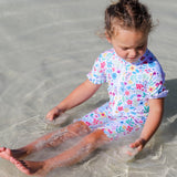 Child in a floral swimsuit playing in shallow water on a beach
