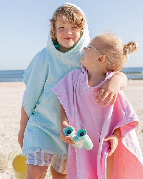 Two children on a beach wearing colorful hooded ponchos