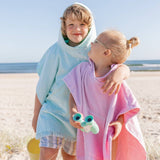 Two children on a beach wearing colorful hooded ponchos