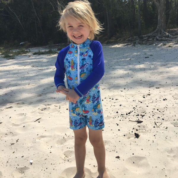 Child wearing a blue koala pattern swimsuit on a sandy beach.