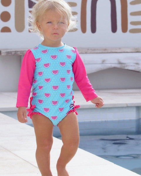 Child wearing a blue and pink swimsuit with watermelon pattern by a pool.