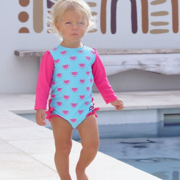 Child wearing a blue and pink swimsuit with watermelon pattern by a pool.