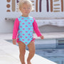 Child wearing a blue and pink swimsuit with watermelon pattern by a pool.