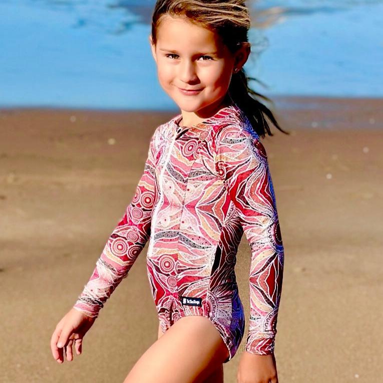 Young girl in a colorful swimsuit standing on a beach.