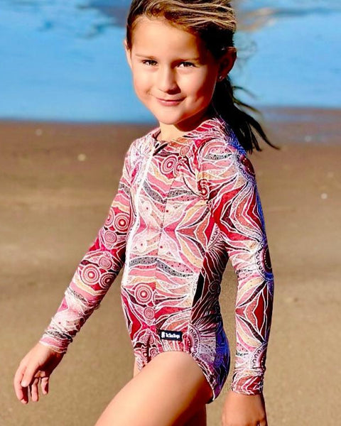 Young girl in a colorful swimsuit standing on a beach.