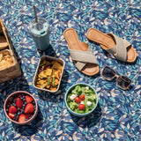 Outdoor setting with sandals, salad, snacks, and a drink on a blue floral tablecloth.