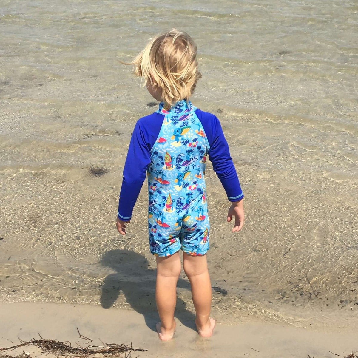 Child wearing a blue one piece long sleave swimsuit with koala patterns on a beach