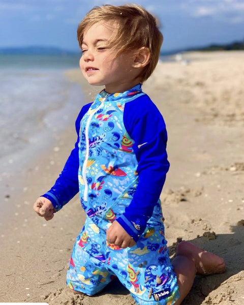 Child wearing a blue koala pattern swimsuit on a sandy beach