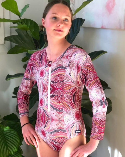 Woman wearing a patterned swimsuit sitting indoors with plants in the background