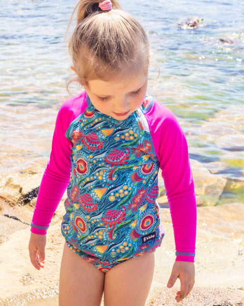 Child wearing a colorful swimsuit with pink sleeves standing on a beach.