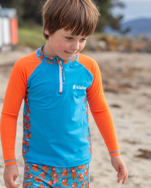 Child wearing a blue and orange shirt with a patterned design on a beach