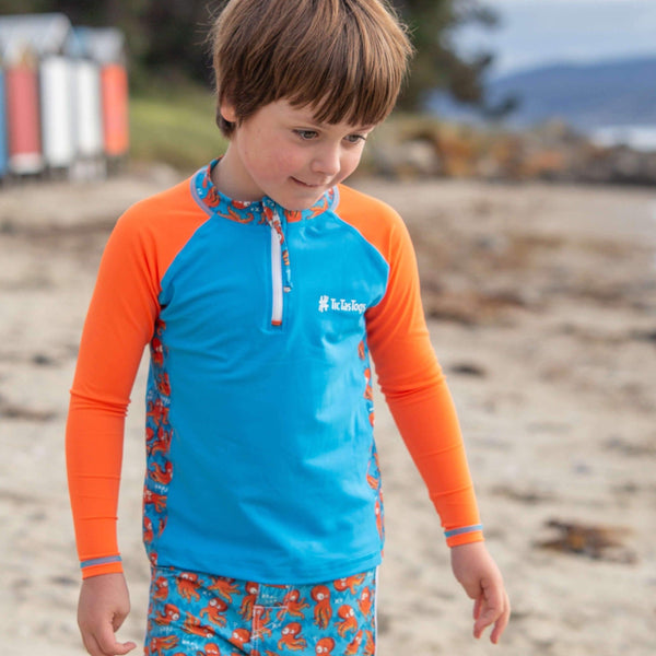 Child wearing a blue and orange shirt with a patterned design on a beach