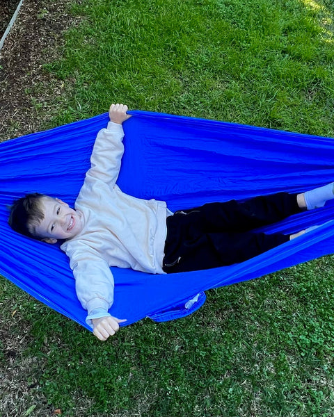 Child lying in a blue hammock on grass