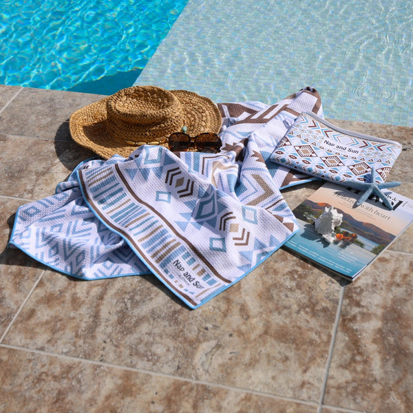 Light blue towel with geometric pattern, straw hat, and wetbag by a poolside.
