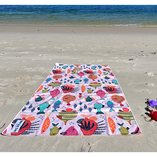 A vibrant kids beach towel with a colorful fish pattern is spread out on the sand at the beach