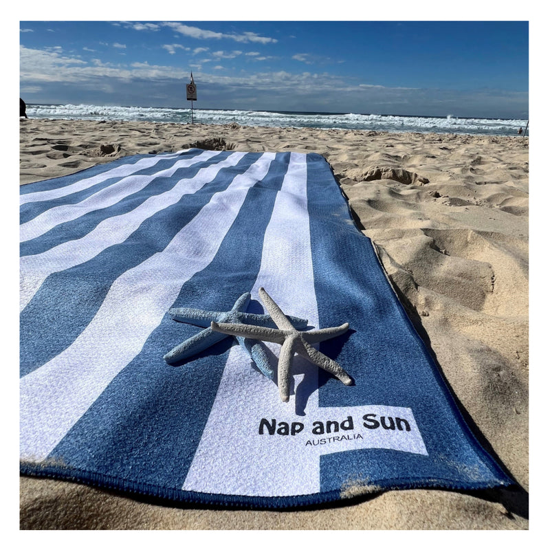 NapandSun Blue and white striped beach towel laying on the soft sand