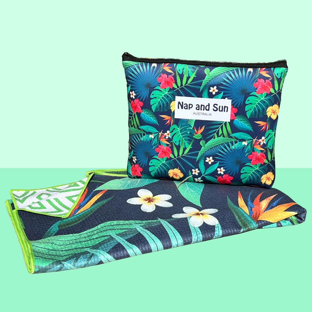 Napandsun Tropical Bliss sand-free beach towel featuring a double-sided design. Front: vivid green tropical leaves with yellow and red hibiscus and white frangipani flowers. Back: white background with green geometric lines. Free matching wet bag is included. This pattern is my personal favorite.