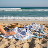 Person with azureblue patterned towel and pouch on a sandy beach 