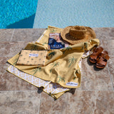 Yellow mustard sand-free towel with palm pattern laid beside a pool, styled with a straw hat and slippers.