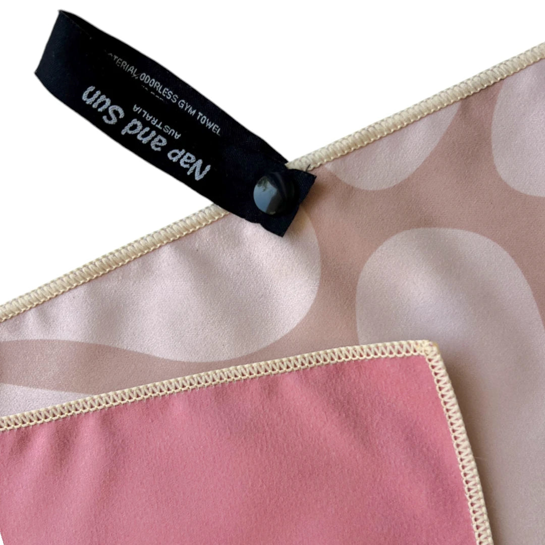 Close-up of Energy gym towel with a nude front featuring a detail of a flower pattern, pink back, and a black hanging loop with 'Nap and Sun Australia' text.