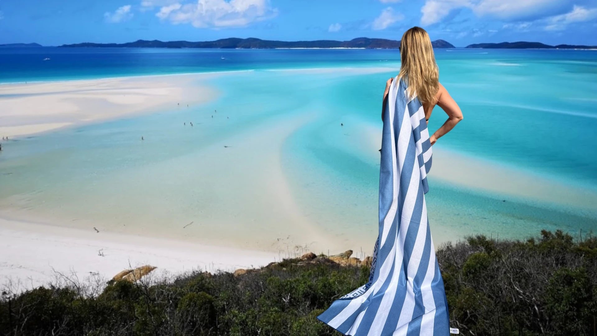  Woman on a hill with a blue and white beach towel, looking at the sea.